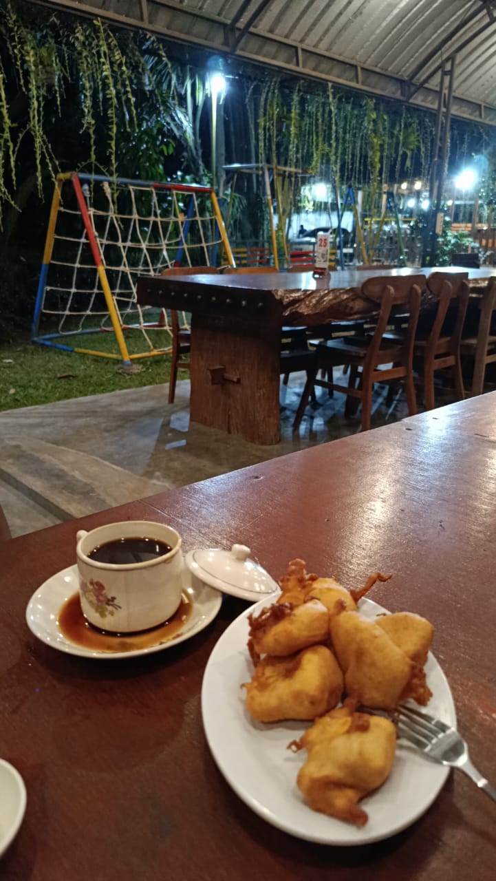 Secangkir kopi dan camilan di meja kayu, dengan area bermain anak di belakangnya